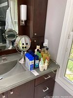 Silver-tone adjustable makeup mirror on bathroom counter with various hair care products around it
