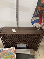 Top-down view of folded brown plastic pet crate showing dog door and items in front including a rolled-up puzzle and an aluminum step or ramp.