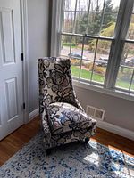 Accent chair placed near window showing front and right side with floral upholstery and dark wooden legs.