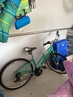 Left side view of teal Specialized mountain bike leaning against wall with camping gear in background