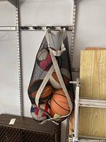 Mesh bag filled with basketballs and volleyballs hanging on a rod in a garage shelf space.