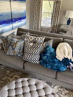 Throw pillows and blankets arranged on a gray sofa, showing patterns and colors.