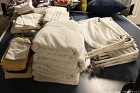 Stack of white body towels, assorted smaller towels in yellow and white, and multiple foldable Oxo drying racks on a table.