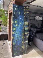 Full view of the large canvas leaning against an exterior wall near a garage showing the textured starry night sky design.