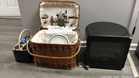 Photo showing the wicker picnic basket with white fabric interior containing plates and flatware and the black Whirlpool microwave placed on the floor