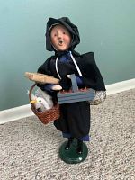 Front view of Byers Choice Caroler figurine showing details of face, clothing, basket with bird, and tray with items.