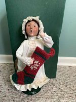 Front view of Byers Choice Caroler figurine, child holding a red and green knitted stocking, standing on a green base.