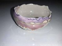 Side angled view of signed pottery bowl showing painted wavy lavender and cream exterior with irregular rim.