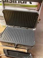 Cuisinart Griddler open showing ribbed reversible grill plates inside, stainless steel body, and front control knob and indicator lights.