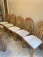 Five wooden dining chairs with curved backs and light gray upholstered seats, lined in a row against wall.