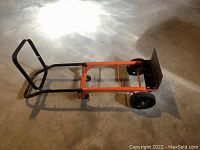 Full side view of the dolly appliance cart showing black handle, orange frame, two large rear wheels, and a flat metal base plate.
