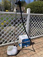 Full view of assembled white Steamfast fabric steamer with collapsible metal column stand and black hose handle with water tank base.
