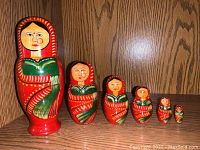 Front view of the set of six red and green hand-painted Indian nesting dolls arranged in descending size order on a wooden shelf.