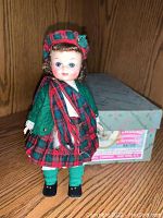 Full body front view of Madam Alexander doll in Scotland attire, showing outfit details and doll's face with original box behind.