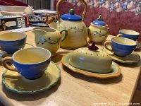 Full view of the tea set laid out on table including cups, saucers, creamer, sugar bowl, butter dish, and metal kettle