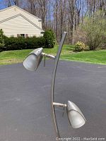 Close-up photo of the metallic cone-shaped lamp heads and part of curved metal stem of the floor lamp in outdoor setting.