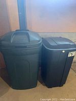 Two plastic trash cans side by side, one dark green and one black.