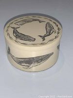Photo of round cream colored trinket box with detailed black whale drawings on lid and side