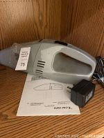 Grey handheld Shark cordless vacuum cleaner with charger and instruction manual, placed on wooden surface
