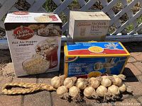 Three boxed small kitchen appliances on pavement: Orville Redenbacher hot air popcorn popper, Sunbeam Hot Shot III hot beverage maker with cup, and European stainless steel meat grinder.