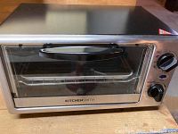 Front view of silver KitchenSmith toaster oven with glass door, black handle, and two control knobs.