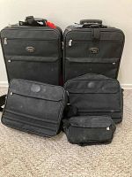 Front view of two black upright rolling suitcases, two shoulder bags, and one small toiletry bag arranged on carpet floor.