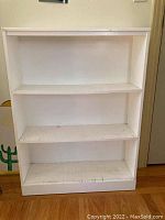 Front view of white wooden shelving unit showing three fixed shelves with worn paint and marks.