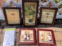 Photo showing all items: three framed wine-themed wall hangings with Fleur de Lis decorations on top, two framed square trivets with wine images, and Stem Grip packaging device on side.