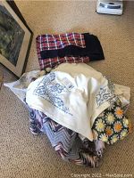 Pile of assorted handmade textile items including afghans, throws, needlepoint, and crochet pieces
