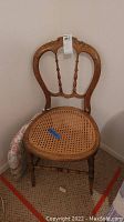 Full view of antique wooden chair with rattan woven seat and carved wooden backrest.