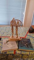 Two wooden articulated human body models on wooden stand with two books lying in front on a patterned table.