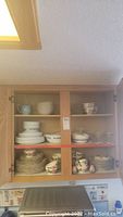 View of upper cabinet shelves showing various dishes and bowls including Corelle Ware and Sunday dishes along with creamer and glass candle holders