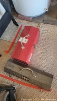 Photo of red and gray metal toolboxes and some tools on carpet floor near water heater.
