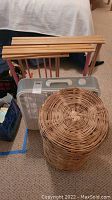 White box fan, two wooden folding clothes drying racks behind it, and tall wicker hamper in front filled with clean rags