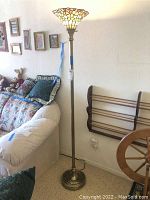 Full view of the tall brass floor lamp with stained glass Tiffany style shade, showcasing floral colored patterns at the top and ribbed brass pole.