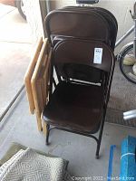 Four brown metal folding chairs stacked together showing padded seats and backs.