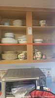 Dinnerware set stored in a cabinet including plates, bowls, cups, and serving dishes, some marked Franciscan Desert Rose pattern.