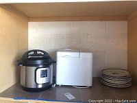 Shelf containing the Instant Pot, bread maker, and stack of plates.