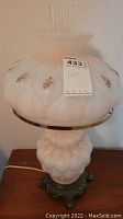 Full view of vintage white glass lamp with floral designs and clear chimney on top, sitting on wood surface.