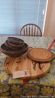Large round Lazy Susan with burnt in design, wood grain visible, placed with nested wood salad bowls and a round cutting board on a floral tablecloth
