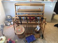 Front view of assembled wooden floor loom with harnesses threaded and fabric basket at base.