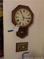 Full view of Seth Thomas wall clock with Roman numerals on octagonal wooden frame and framed World Map wall art below it.