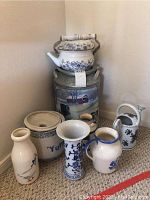 Overview photo showing all ceramic pitchers, vases, teapot, large painted milk can, and ceramic crock grouped together on carpeted floor.