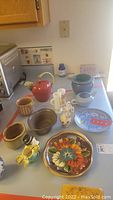 Overview of all ceramic items laid out on table including pitcher, creamer, plates, duck figurine, nut dish and bowls