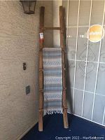 Full view of rustic wood ladder standing upright with woven blanket draped over rungs, showing color and texture details of both items.
