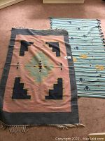 Two small rugs on carpet floor; one with Southwestern geometric pattern and the other with striped abstract floral/sun motifs.