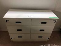 Front view of the white 6 drawer dresser with black handles and smooth top surface