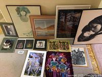 12 various framed and unframed art pieces on floor including portraits, landscape, batik, photographs and prints.