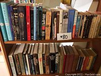 Shelf with multiple novels and autobiographical books including The Dukan Diet, The Lost City of Z, and others with a price tag $80