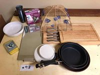Full view of lot items including pans, cutting board and utensils, bamboo food cover, scale, travel mug, vintage tin, mirror, lightbulbs, and dish bowl